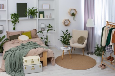Photo of Stylish bedroom with comfortable bed, clothes rack and different houseplants. Interior design