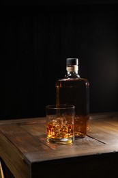 Photo of Whiskey with ice cubes in glass and bottle on wooden crate against black background