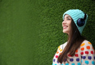 Photo of Beautiful young woman listening to music with headphones near grass wall. Space for text