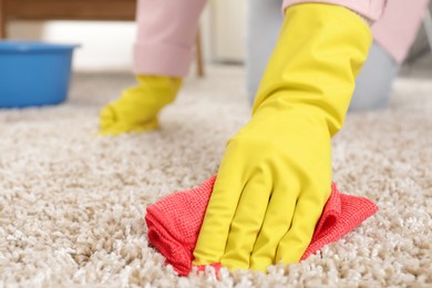 Woman in rubber gloves cleaning carpet with rag indoors, closeup. Space for text