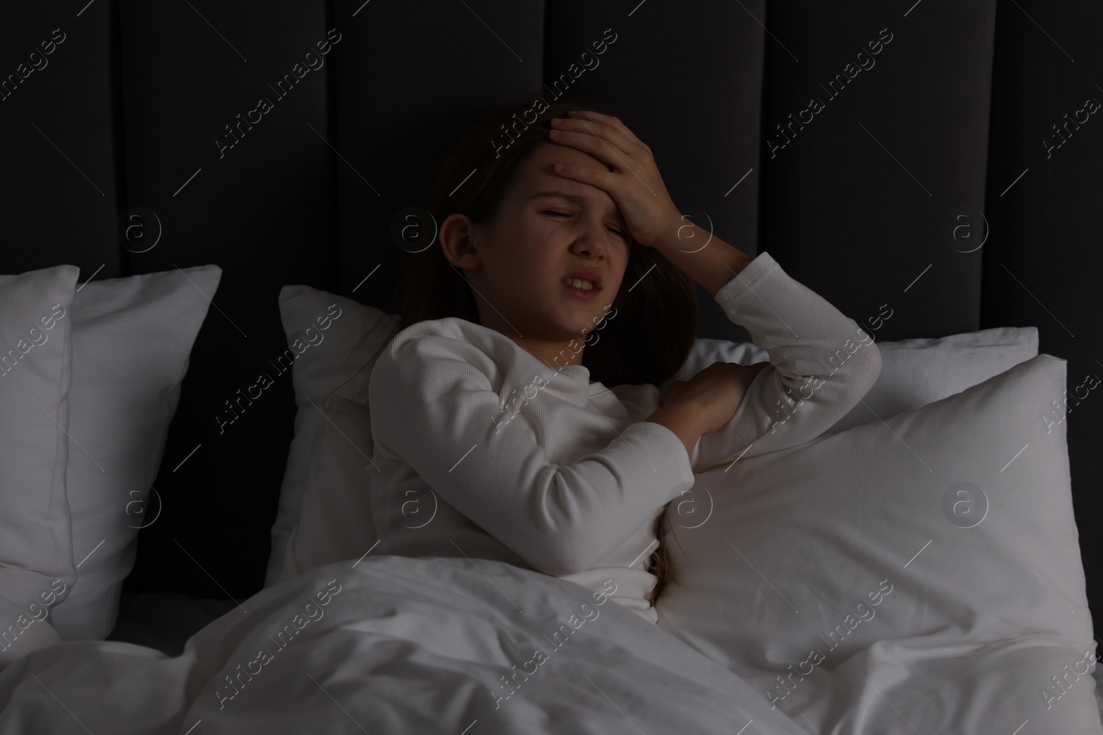 Photo of Little girl suffering from headache in bed at night