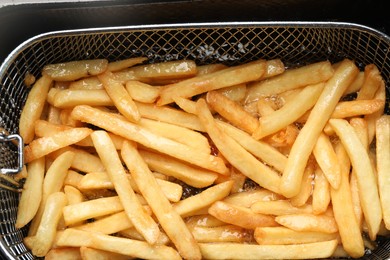 Cooking delicious french fries in hot oil, closeup