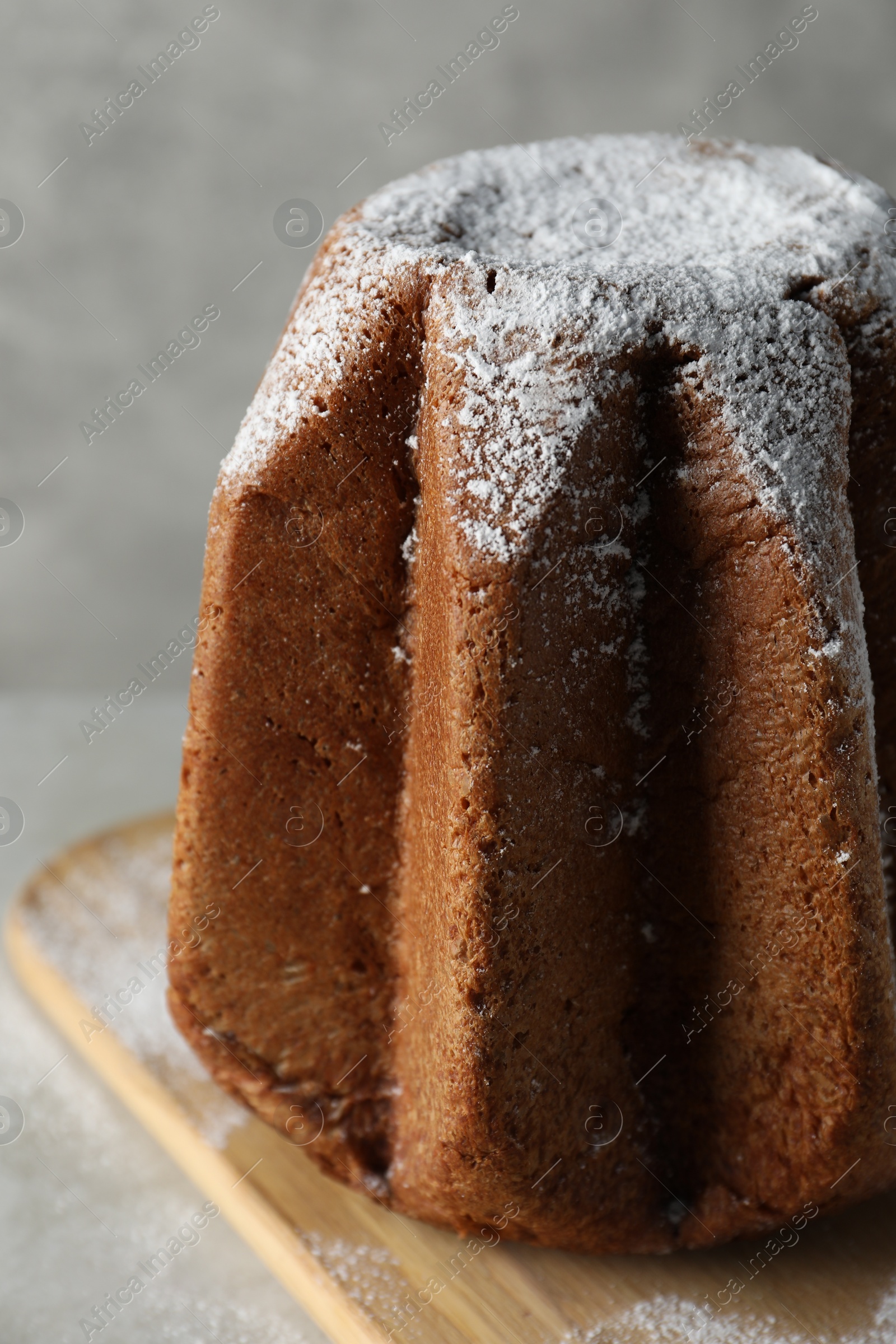 Photo of Delicious Pandoro cake decorated with powdered sugar on light grey table, closeup. Traditional Italian pastry