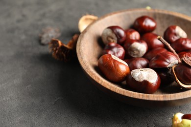 Photo of Horse chestnuts in wooden bowl on grey table, closeup