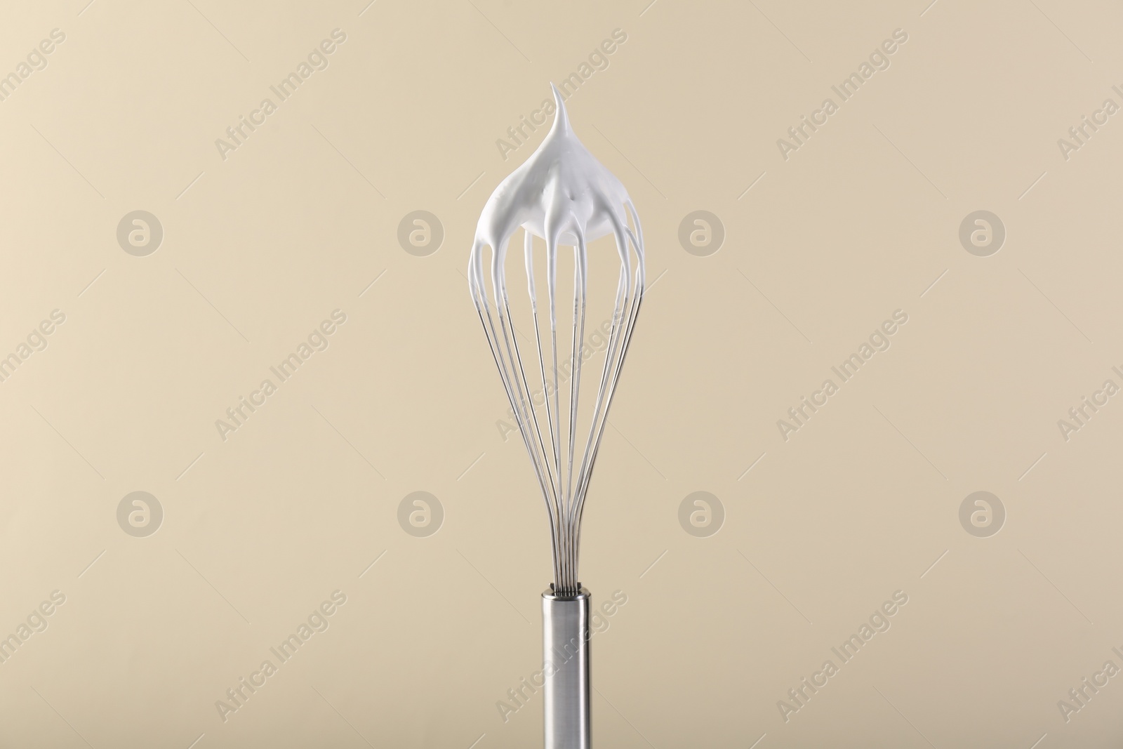 Photo of Whisk with whipped cream on beige background