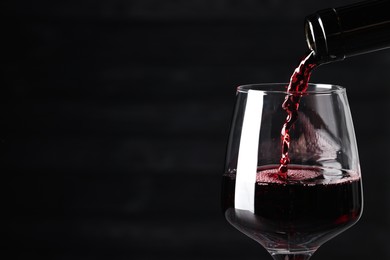 Photo of Pouring red wine into glass against dark background, closeup. Space for text