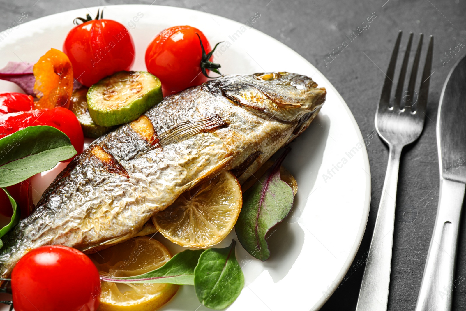 Photo of Delicious roasted fish with lemon and vegetables on dark grey table, closeup