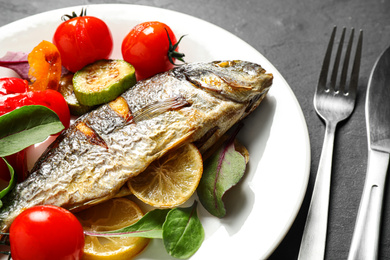 Photo of Delicious roasted fish with lemon and vegetables on dark grey table, closeup