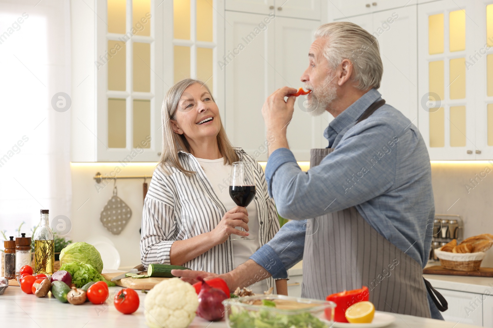 Photo of Happy senior couple cooking together in kitchen. Woman with glass of wine near her husband