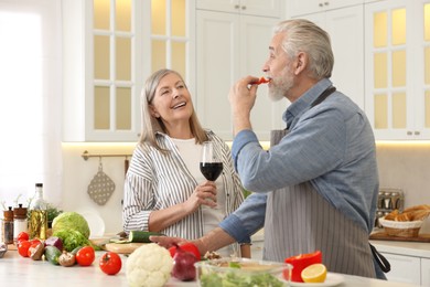 Photo of Happy senior couple cooking together in kitchen. Woman with glass of wine near her husband