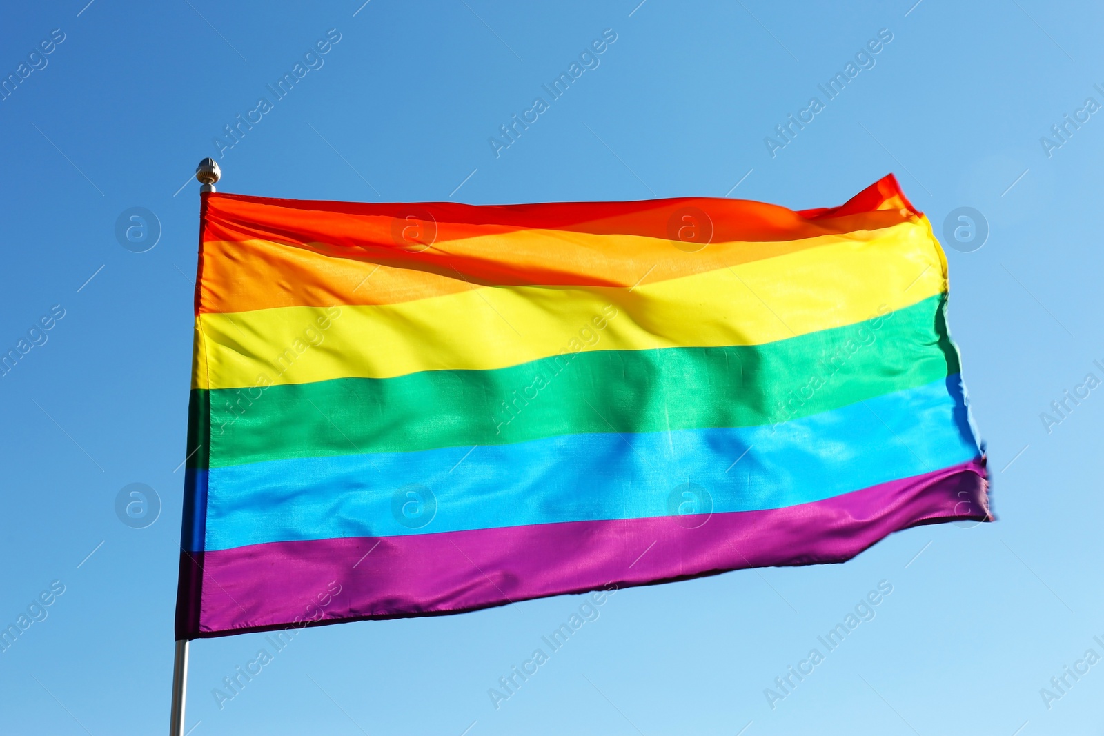 Photo of Rainbow LGBT flag fluttering on blue sky background. Gay rights movement