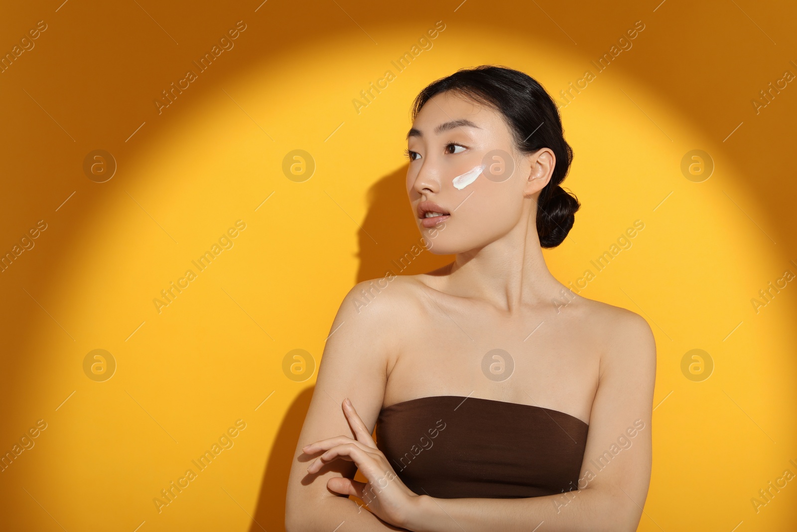 Photo of Beautiful young woman in sunlight with sun protection cream on her face against orange background, space for text