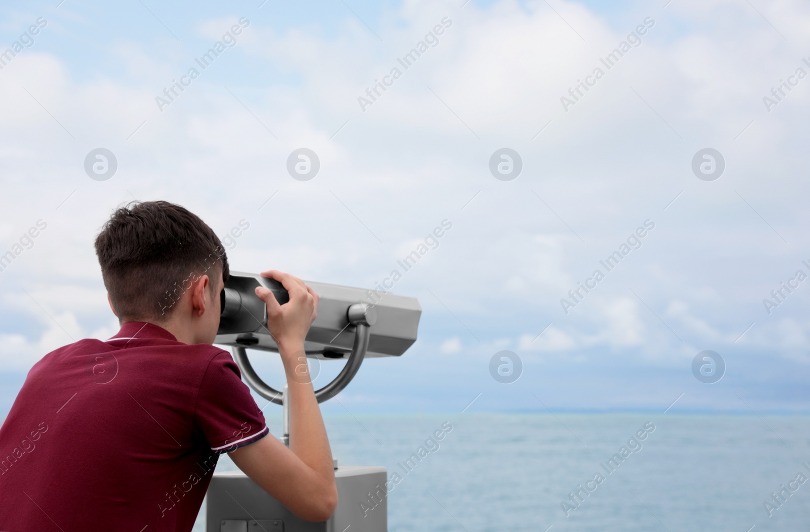 Photo of Teenage boy looking through mounted binoculars at mountains. Space for text