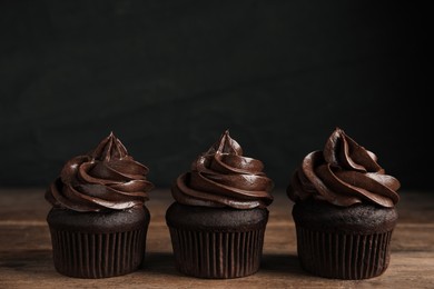Photo of Delicious chocolate cupcakes with cream on wooden table against dark background. Space for text