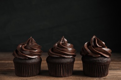 Delicious chocolate cupcakes with cream on wooden table against dark background. Space for text