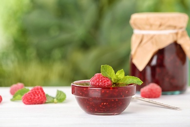 Bowl with raspberry jam on table against blurred background