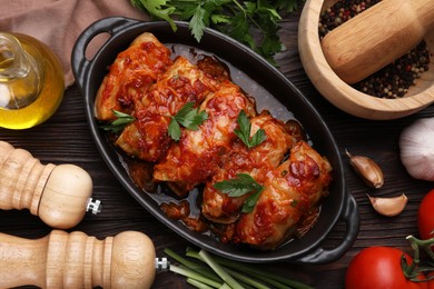 Delicious stuffed cabbage rolls cooked with tomato sauce and ingredients on wooden table, flat lay