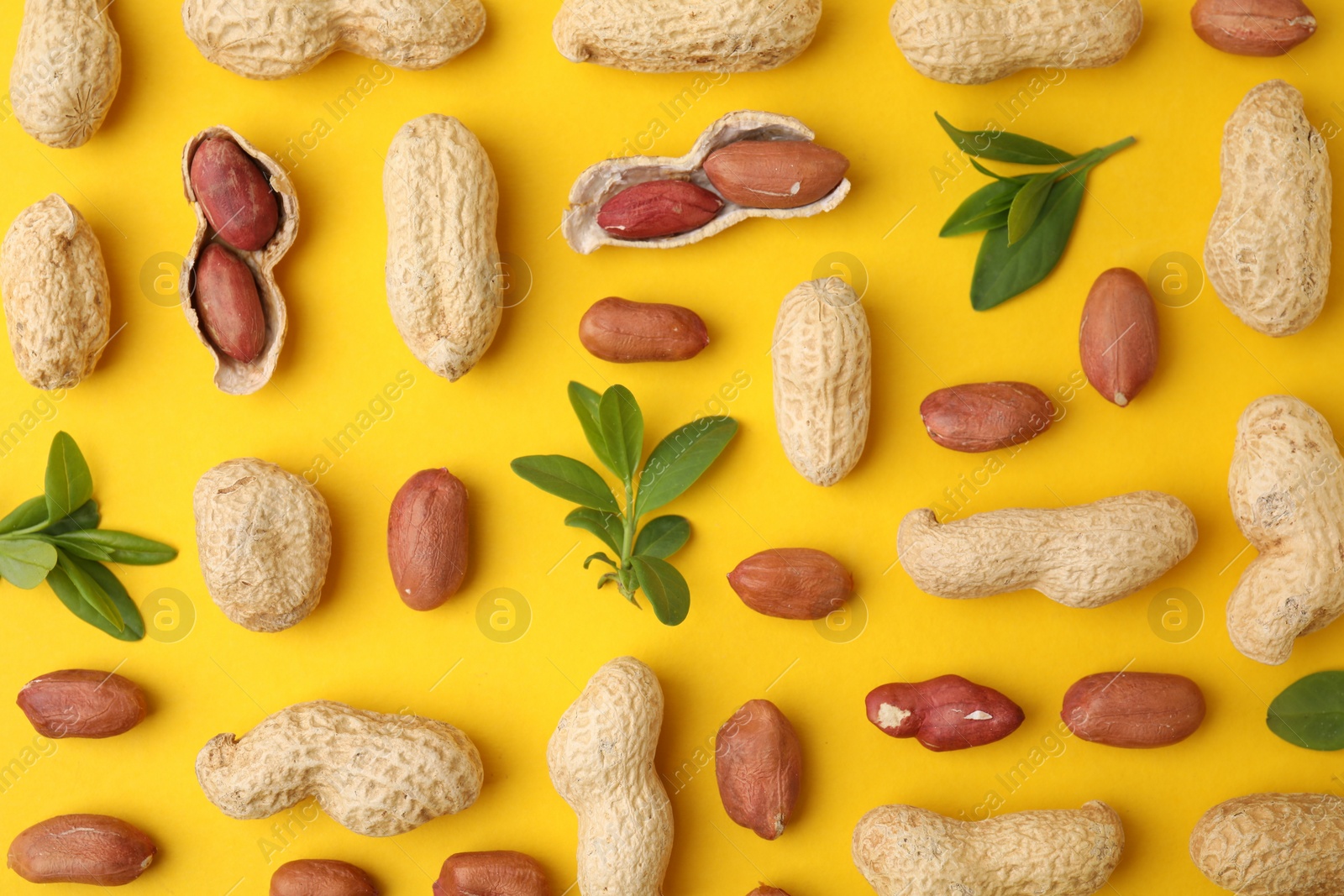 Photo of Fresh peanuts and leaves on yellow table, flat lay