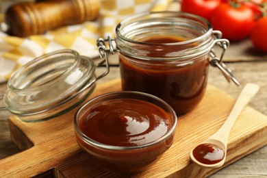 Tasty barbeque sauce in bowl, jar and spoon on wooden table, closeup