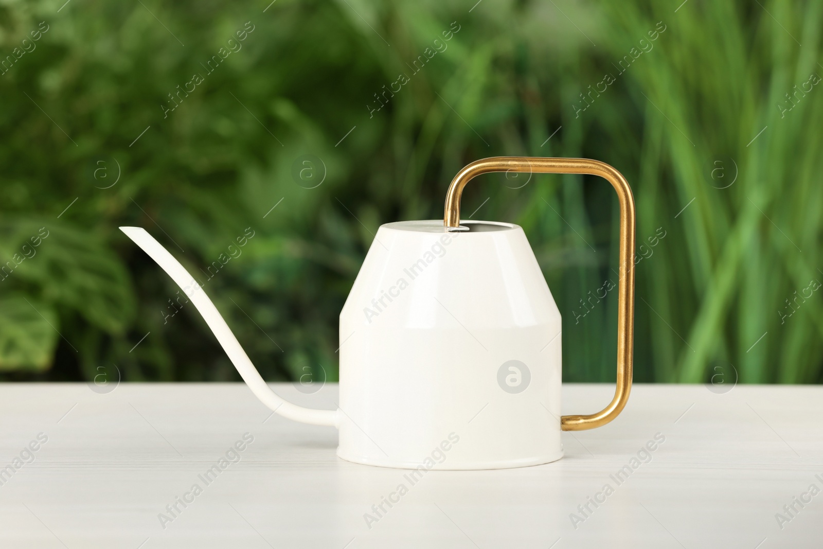 Photo of Stylish watering can on white table against blurred background