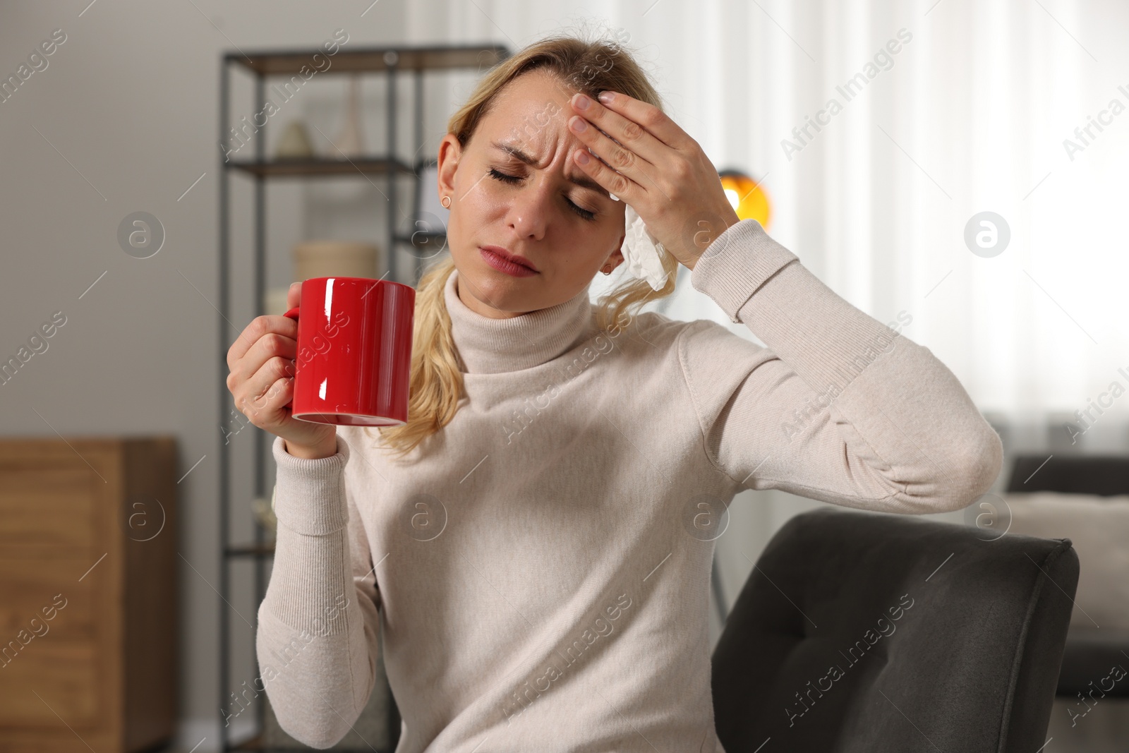 Photo of Sick woman with cup of drink in armchair at home. Cold symptoms