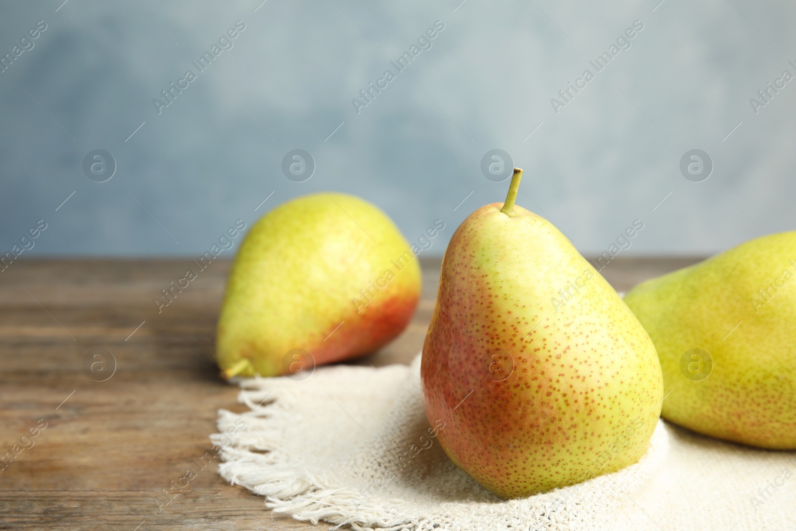 Photo of Ripe juicy pears on brown wooden table against blue background. Space for text