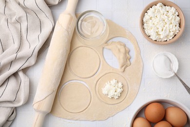 Photo of Process of making dumplings (varenyky) with cottage cheese. Raw dough and other ingredients on white tiled table, flat lay