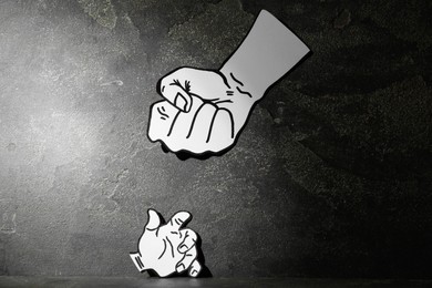 Stop child abuse. Paper cutout in shape of parent's fist above kid's hand on grey textured background
