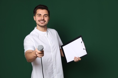 Young man in casual clothes holding microphone and clipboard on color background. Space for text