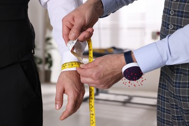 Photo of Professional tailor measuring client's wrist circumference in atelier, closeup
