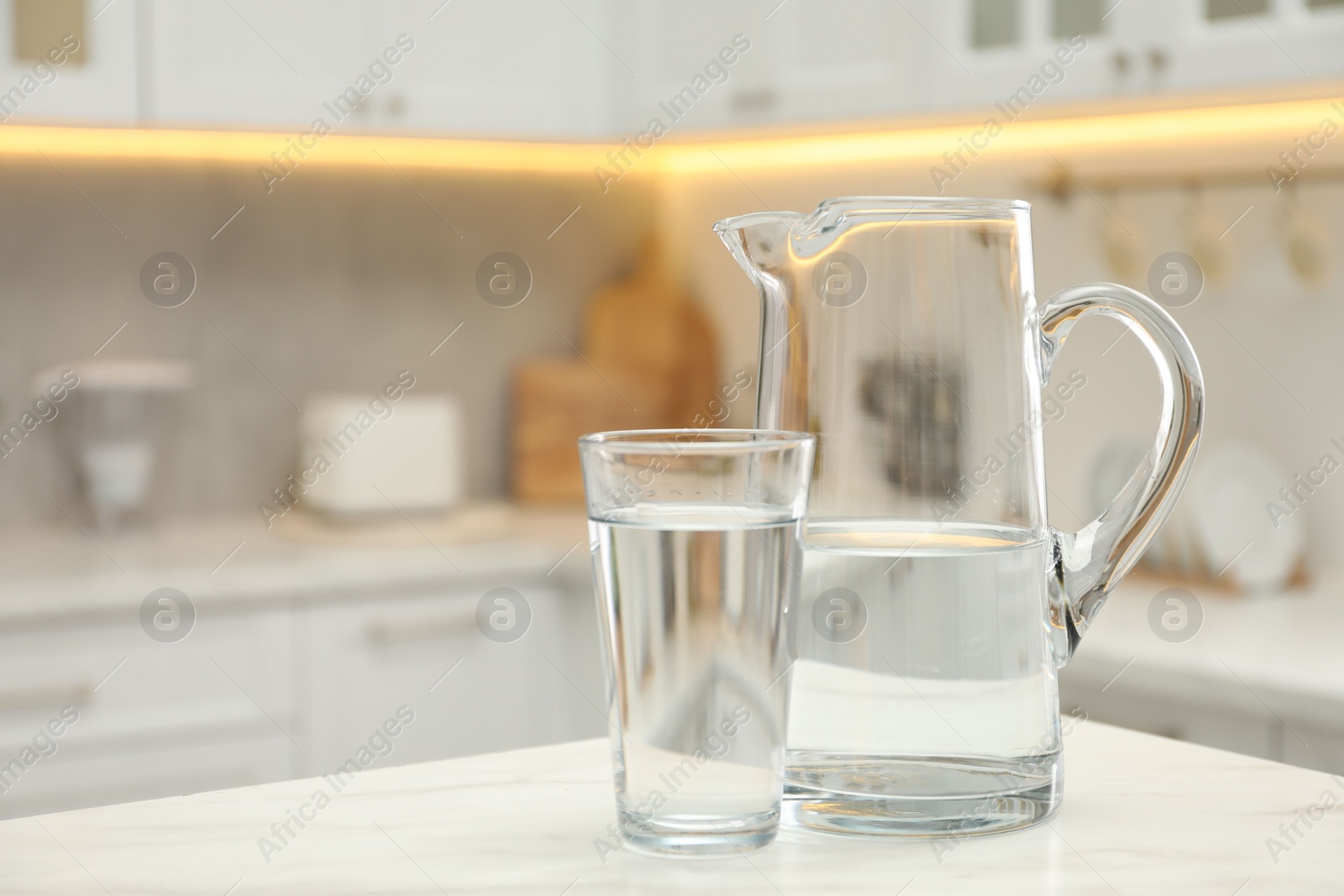 Photo of Jug and glass with clear water on white table in kitchen, space for text