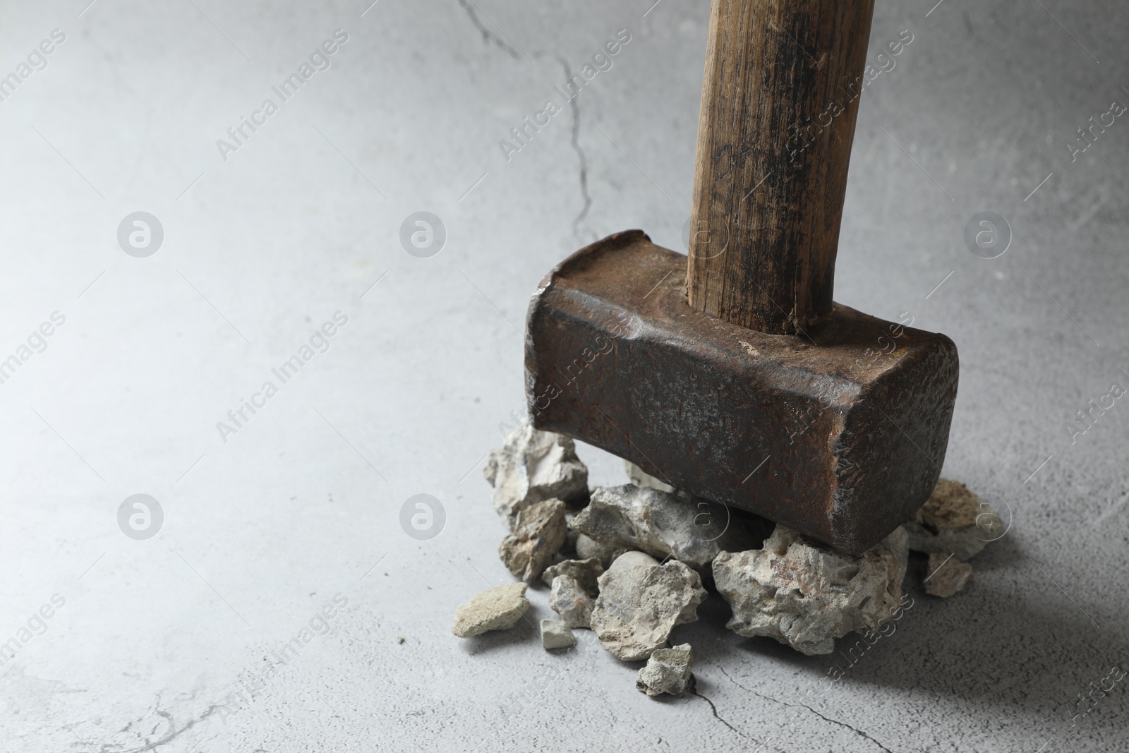 Photo of One sledgehammer and pieces of broken stones on grey background, closeup. Space for text