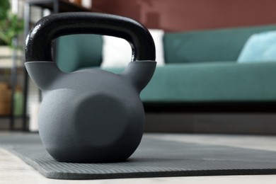 Kettlebell and grey yoga mat on floor in room. Space for text