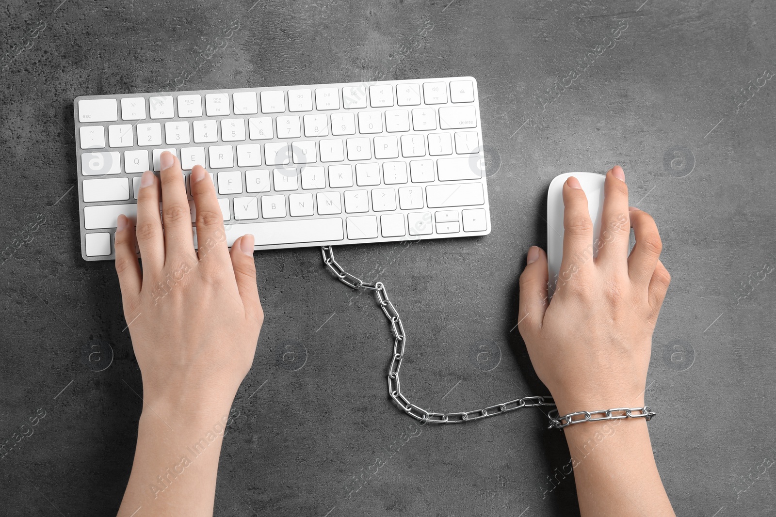 Photo of Woman chained to computer keyboard at grey table, top view. Loneliness concept