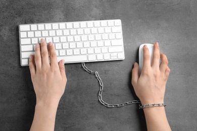 Photo of Woman chained to computer keyboard at grey table, top view. Loneliness concept