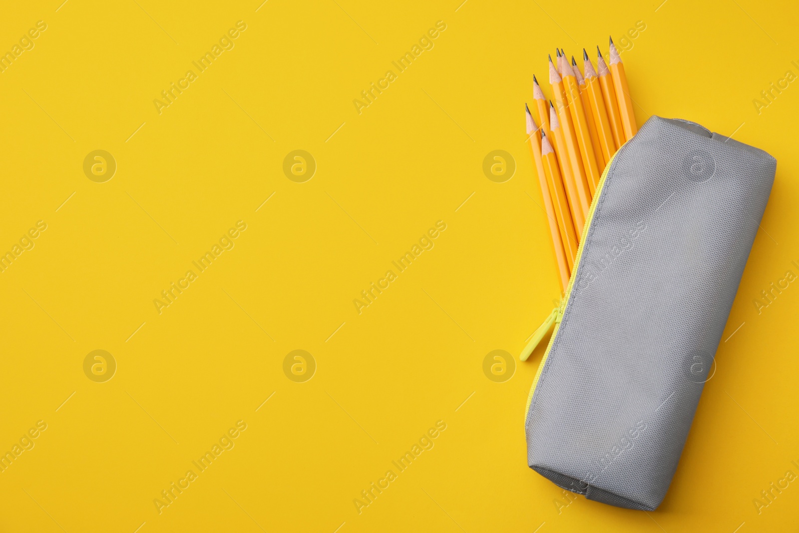 Photo of Many sharp pencils in pencil case on yellow background, top view. Space for text