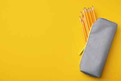 Photo of Many sharp pencils in pencil case on yellow background, top view. Space for text