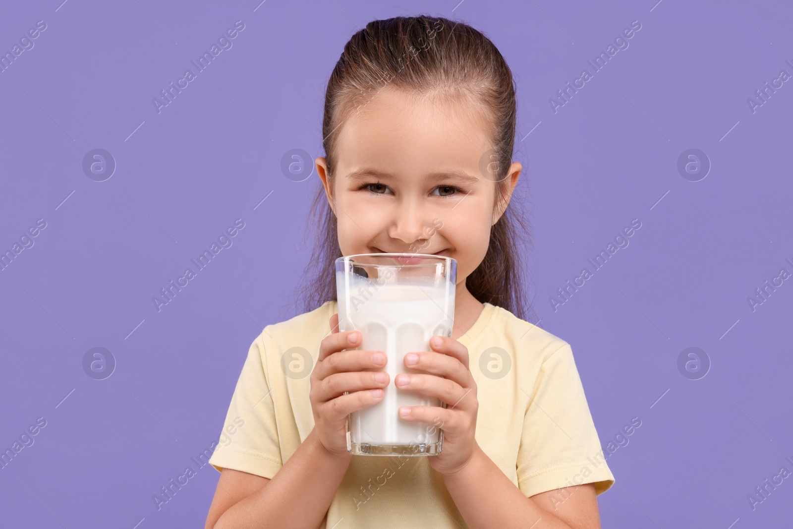 Photo of Cute girl with glass of fresh milk on violet background