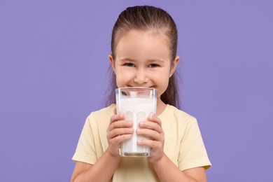 Photo of Cute girl with glass of fresh milk on violet background