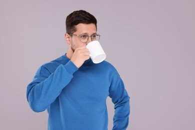 Man drinking from white mug on grey background. Space for text