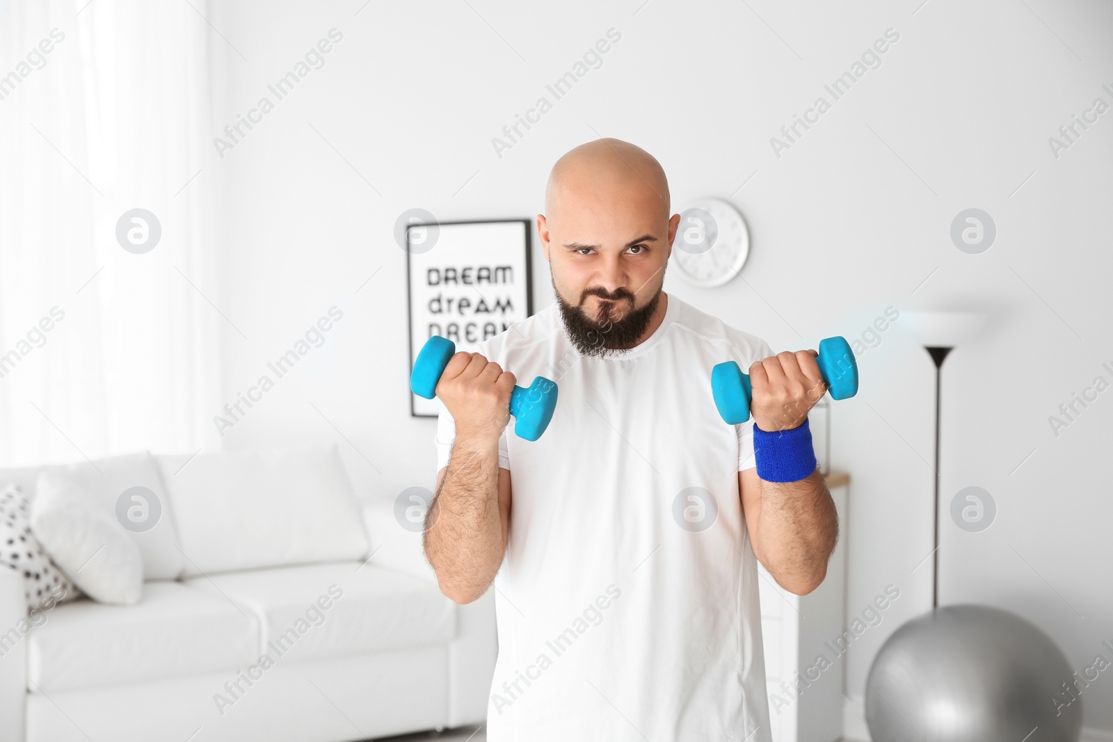 Photo of Overweight man doing exercise with dumbbells at home