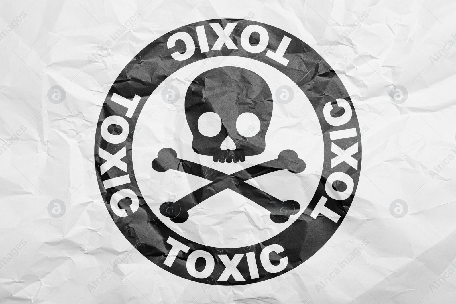 Image of Hazard warning sign (skull-and-crossbones symbol and word TOXIC) on crumpled white paper, top view