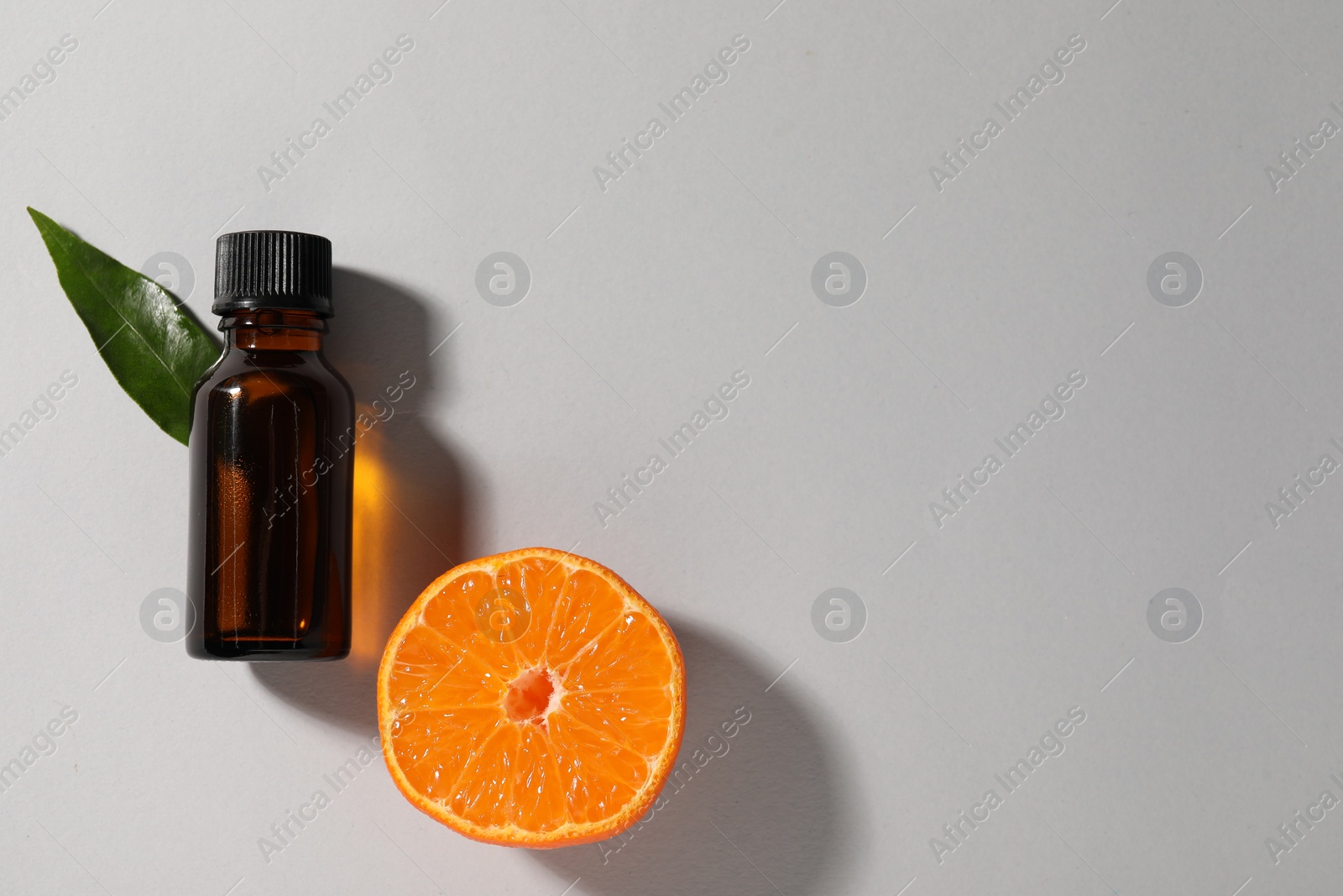 Photo of Aromatic tangerine essential oil in bottle, leaf and citrus fruit on grey table, top view. Space for text