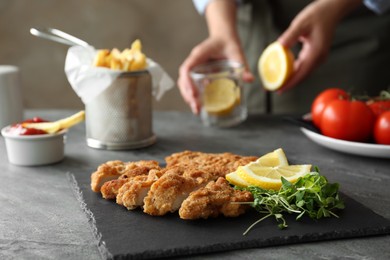 Photo of Tasty schnitzel served with microgreens and lemon on grey table, closeup