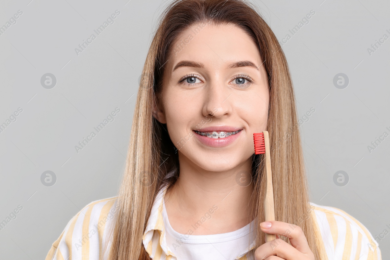 Photo of Portrait of smiling woman with dental braces and toothbrush on grey background