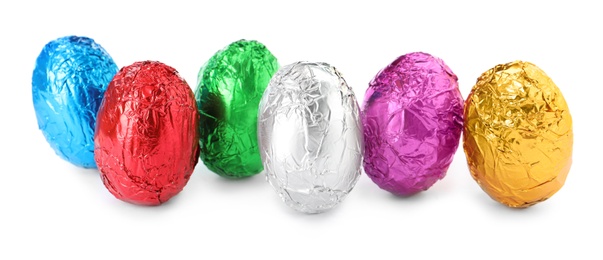 Photo of Many chocolate eggs wrapped in bright foil on white background