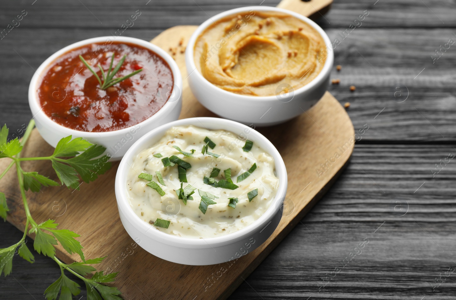 Photo of Different tasty sauces in bowls and parsley on black wooden table, closeup