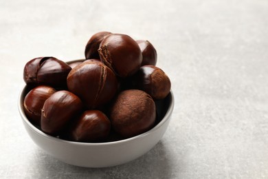 Fresh edible sweet chestnuts in bowl on grey table. Space for text