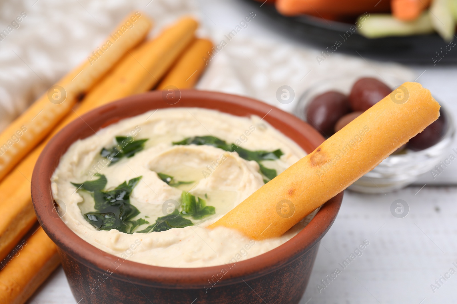 Photo of Delicious hummus with grissini sticks on white wooden table, closeup