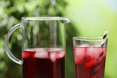 Refreshing hibiscus tea with ice cubes on blurred green background, closeup